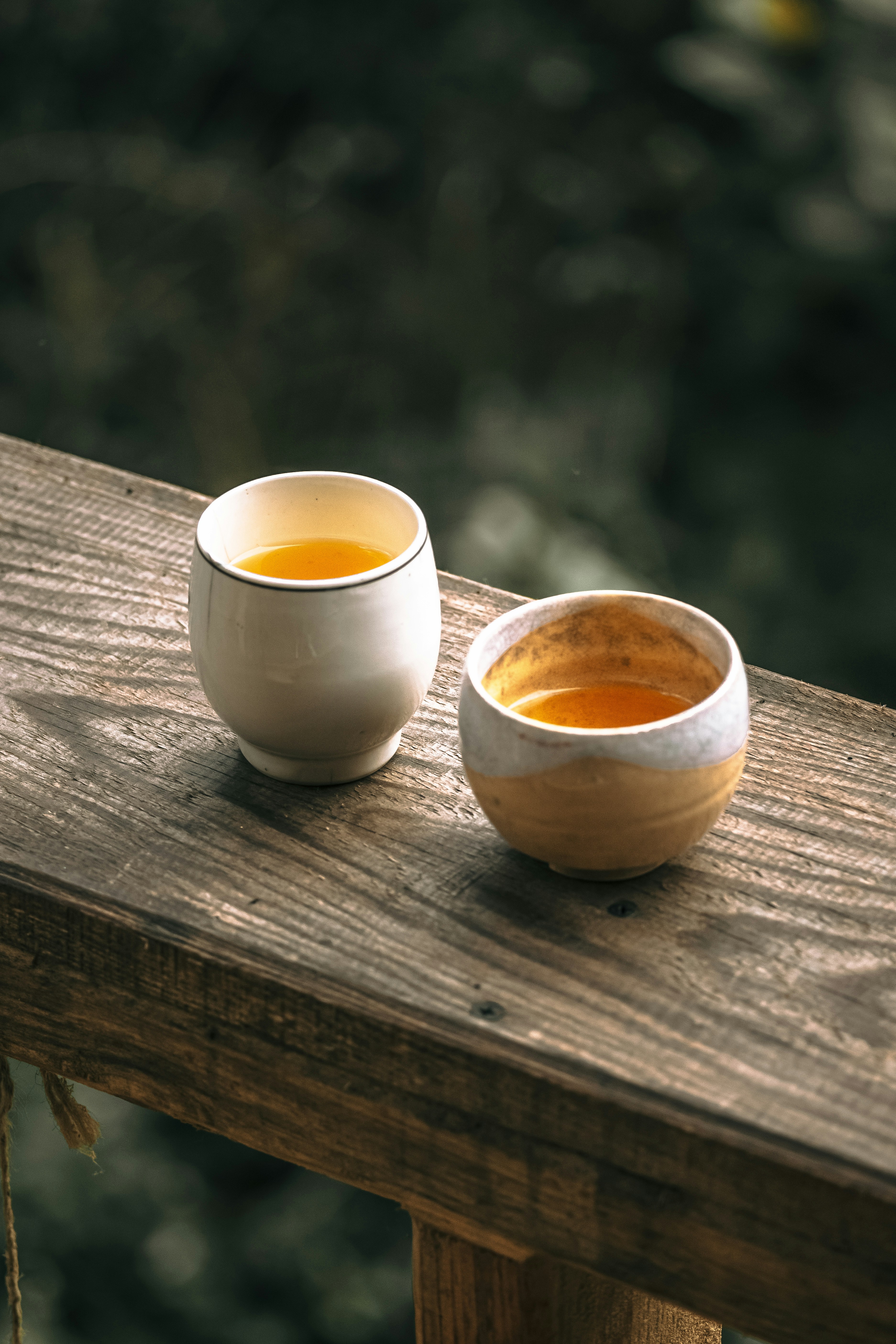 Two warm cups of tea resting on a wooden bench